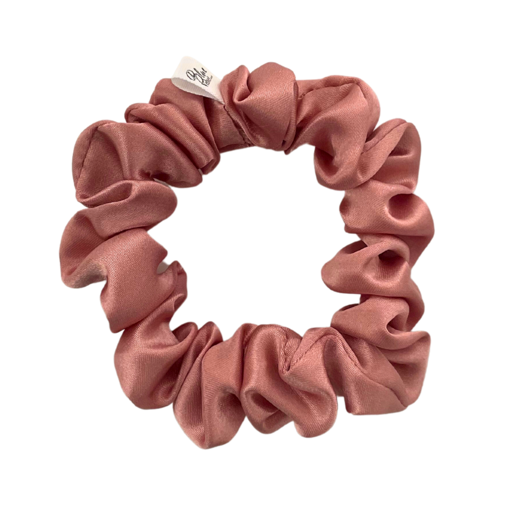 A dusty pink satin scrunchie displayed on a white background.