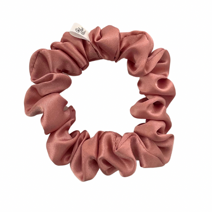 A dusty pink satin scrunchie displayed on a white background.