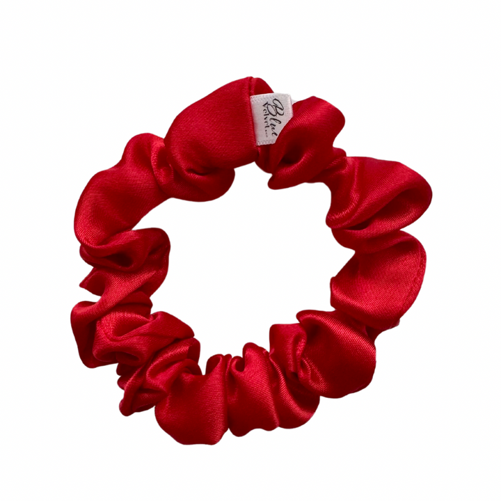 A bold red silky satin scrunchie against a white background.